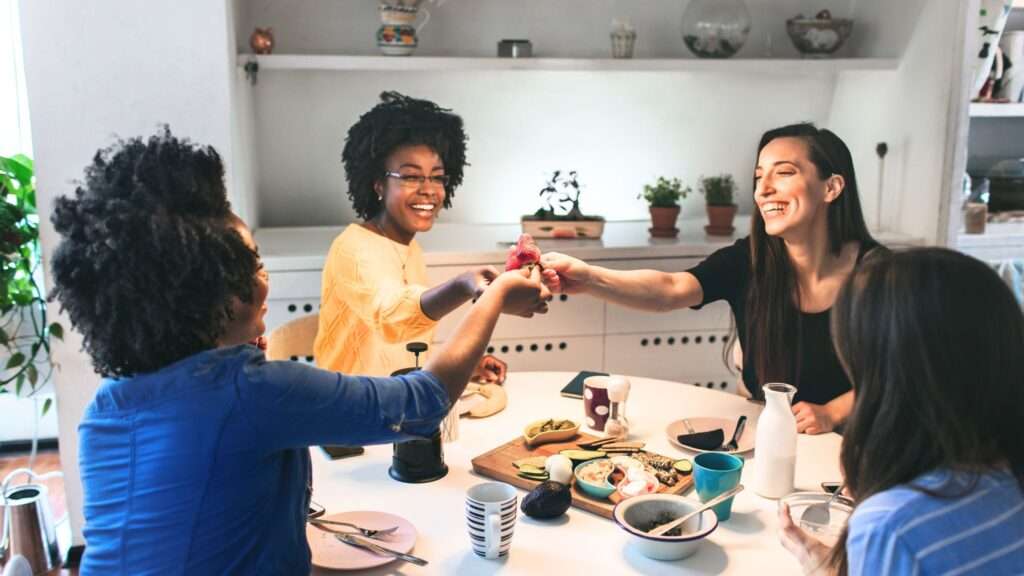 A group of 4 women around a table toasting with glasses raised up.