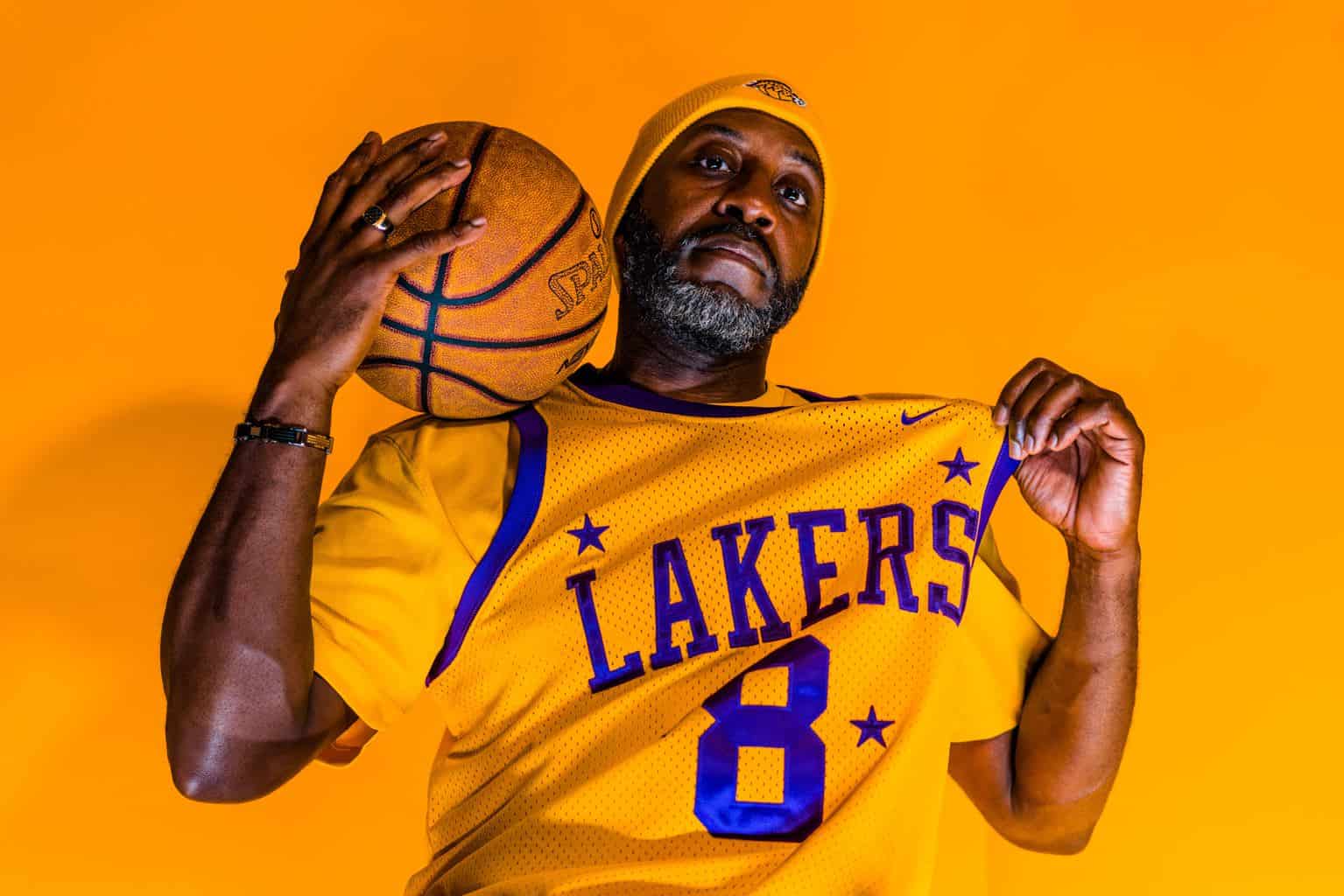 Man in Lakers jersey holding basketball on shoulder