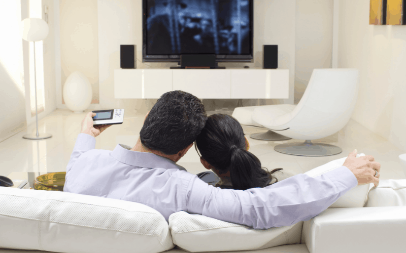 A male and female couple sitting on a couch watching TV