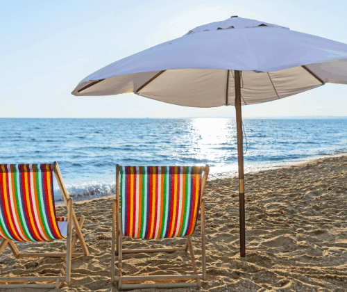 Two beach chairs and a 
beach umbrella on the sand near the ocean. 
