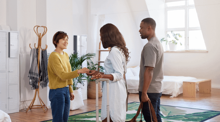Woman welcoming black female and male, handing them a set of keys. 