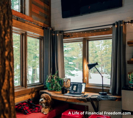 Room in a room with windows showing the snow outside. Laptop on desktop and a dog is on the seat bench by the window.