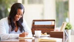 smiling woman at a table writing in a writing pad. smiling woman at a table writing in a writing pad. Affiliate Marketing writing on white paper and pinned to a corkboard. Close up shot of a woman holding money in both hands. 25 Ways to Earn Real Money From Home