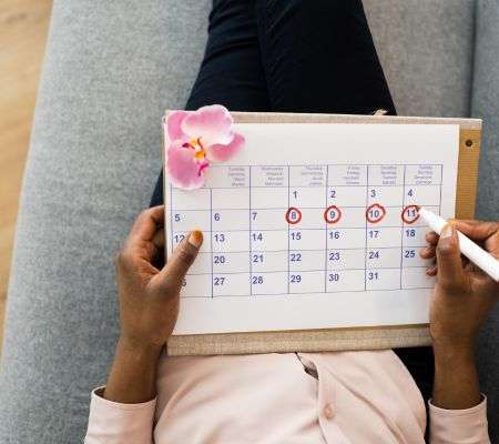 woman with a calendar in her lap, circling dates on a calendar. 